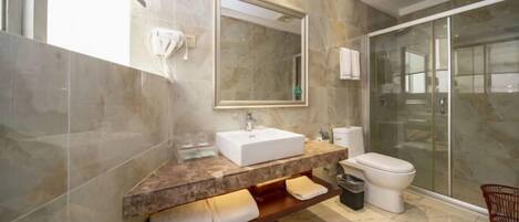 A modern bathroom with a marble vanity, a large mirror, a toilet, and a glass shower enclosure.