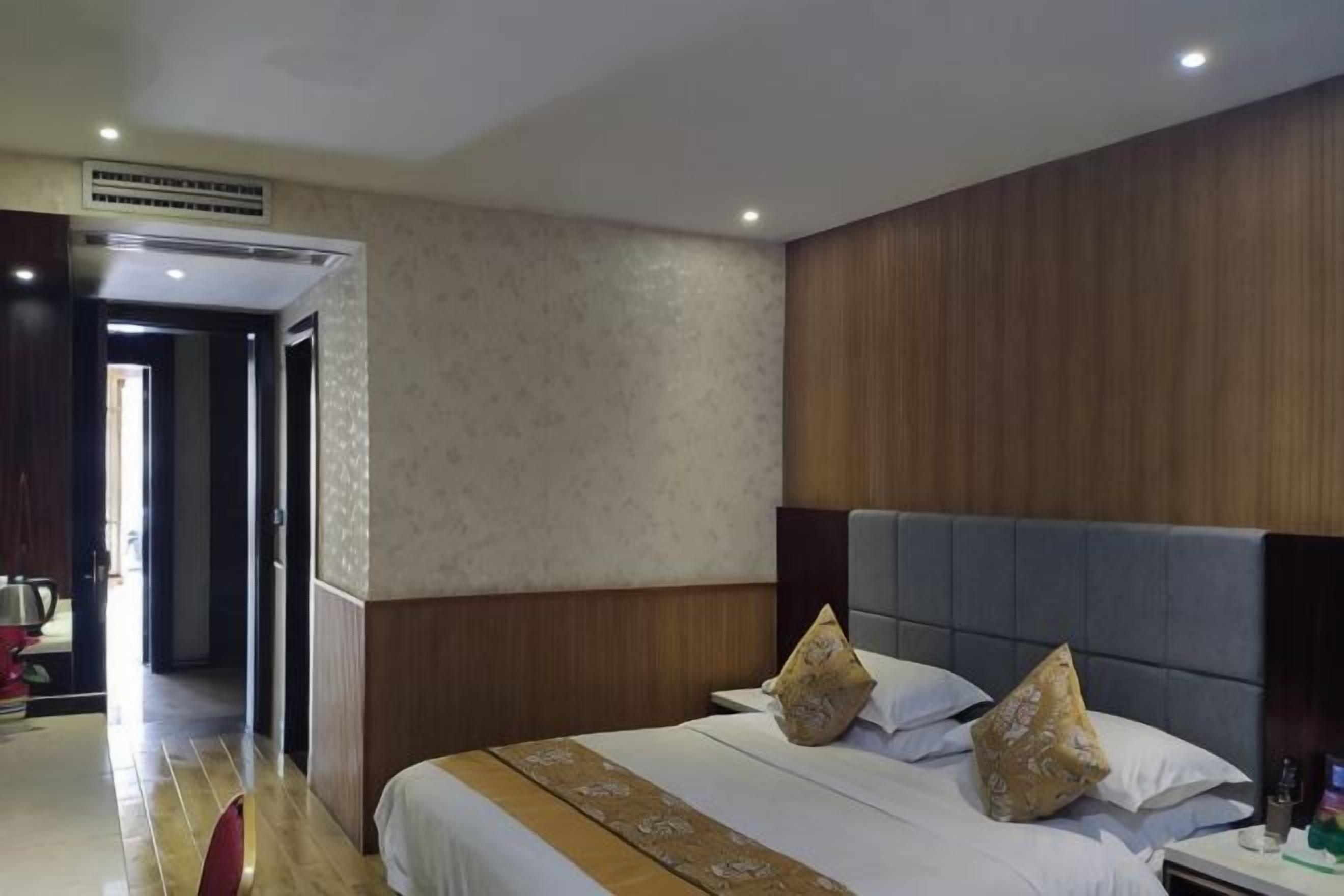A hotel room with a large bed, a wooden headboard, and a visible door leading to another room.