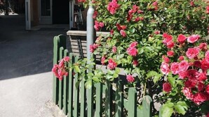 Un edificio de fachada color beige, con una entrada visible y una cerca verde adornada con flores rosadas.