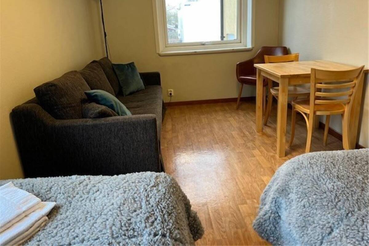 Een knus woongedeelte met een bank, een eettafel met stoelen, een lamp en een raam.