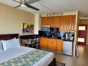 A hotel room with a bed, a kitchenette, a ceiling fan, and a painting on the wall. - Unbeatable views! Recently renovated studio Kitchenette, WiFi–Waikīkī Shore 604 (HONOLULU)