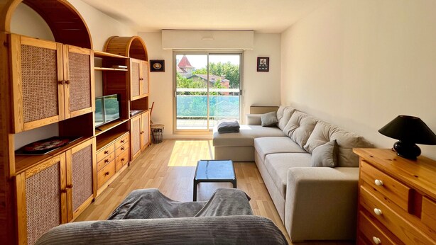A cozy living room with a sofa, a wooden cabinet, and a television. - "Charming Apt near Casino & Beach, Parking, Balcony, Shops Nearby" (Arcachon)