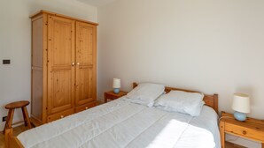 A bedroom with a large wooden wardrobe, a single bed with white bedding, two bedside tables with lamps, and a small stool. - "Charming Apt near Casino & Beach, Parking, Balcony, Shops Nearby" (Arcachon)