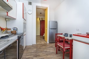 A compact kitchen with a dishwasher, a refrigerator, and a dining area with red chairs.