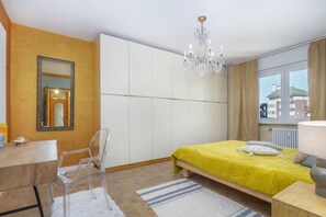 Ein Hotelzimmer mit Bett, Schreibtisch, Stuhl, einer Kandelaber und einem Vorhangfenster.