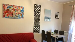 Un salon avec un canapé rouge, une table à manger avec des chaises et un panneau décoratif.