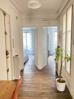 Un pasillo con piso de madera, puertas blancas y una planta en maceta.
