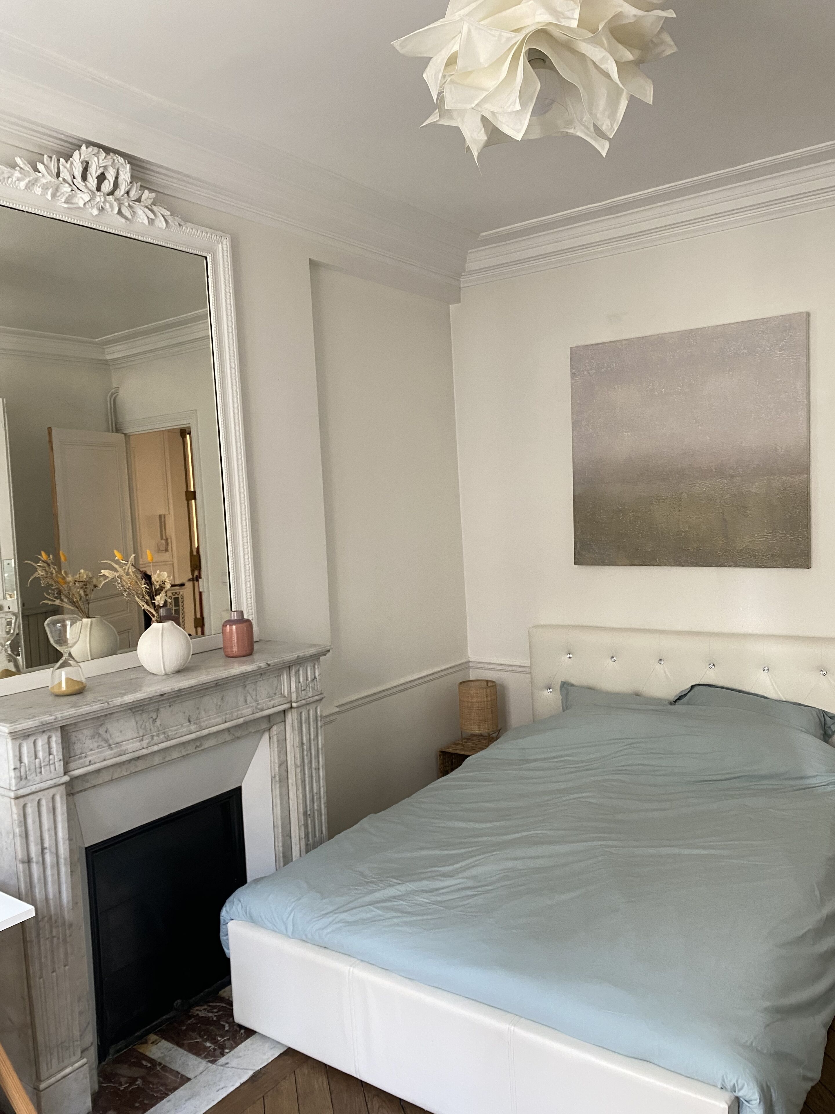 Ein Schlafzimmer mit einem Bett, einem Kamin, einem großen Spiegel und einem Bild an der Wand.