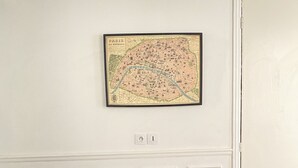 Een kamer met een houten tafel, twee oranje stoelen, een inlijsting kaart aan de muur, en een witte deur.