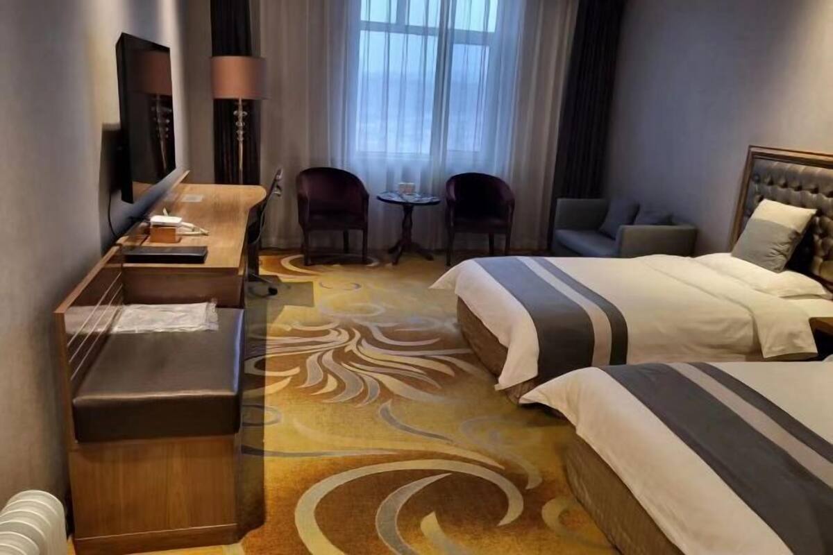 A hotel room with a bed, a desk, a chair, a small table, and a TV.