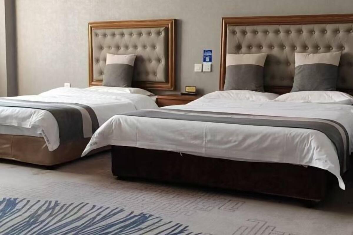 A hotel room with two beds, each with a tufted headboard and white bedding.