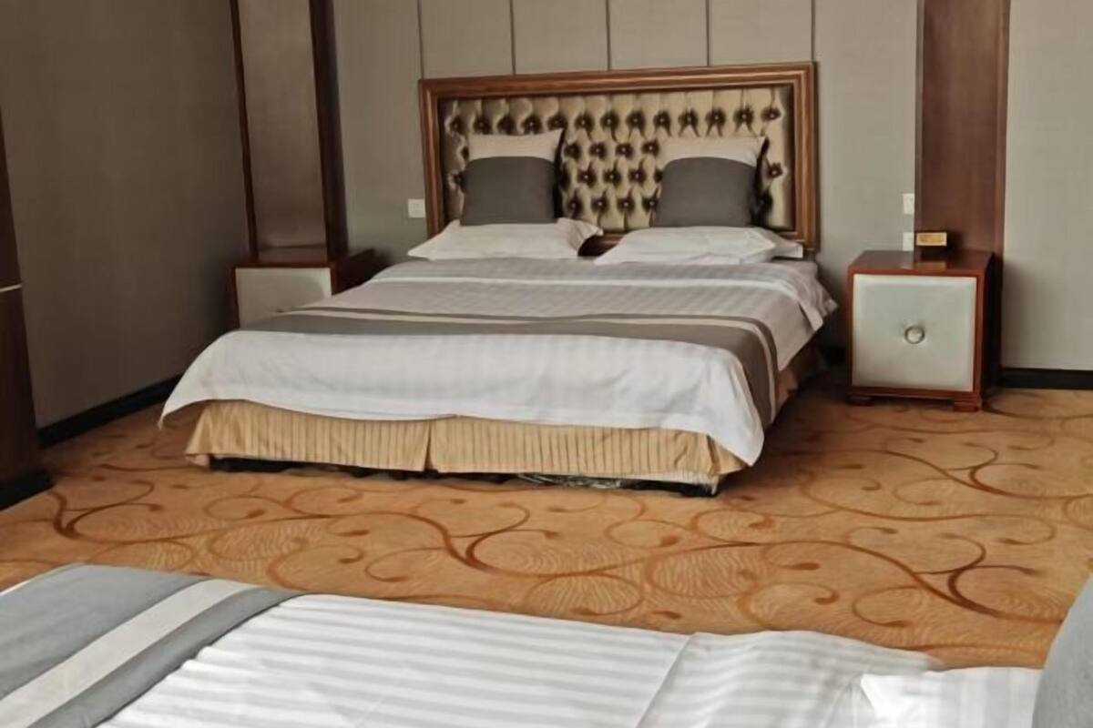 A neatly made double bed with a patterned headboard, a bedside table with a lamp, and a carpeted floor.