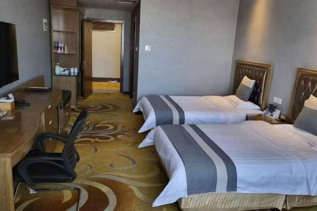 A hotel room with two beds, a TV, a desk, and a chair.