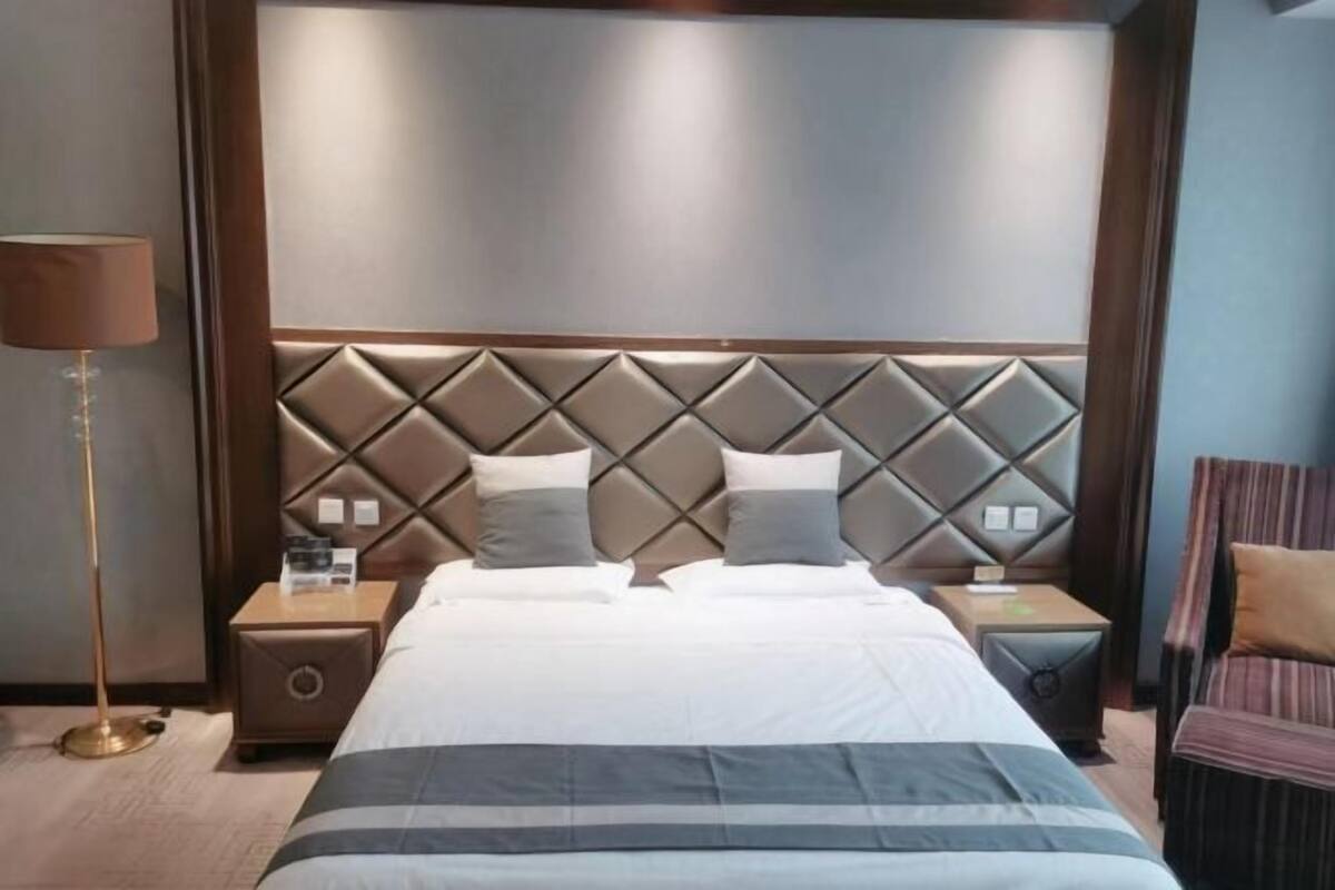 A hotel room with a large bed, a headboard with a diamond pattern, two bedside tables with lamps, and a striped chair.