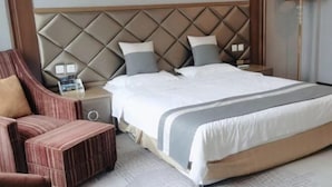 A hotel room with a large bed, a padded headboard, a nightstand, a chair, and a lamp. - Jinjiang Business Hotel (Yilan)