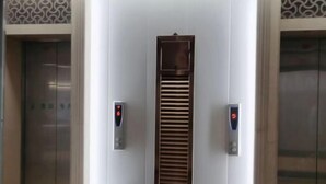 An elevator with two control panels on either side, a central panel with horizontal slats, and a trash bin to the left. - Jinjiang Business Hotel (Yilan)