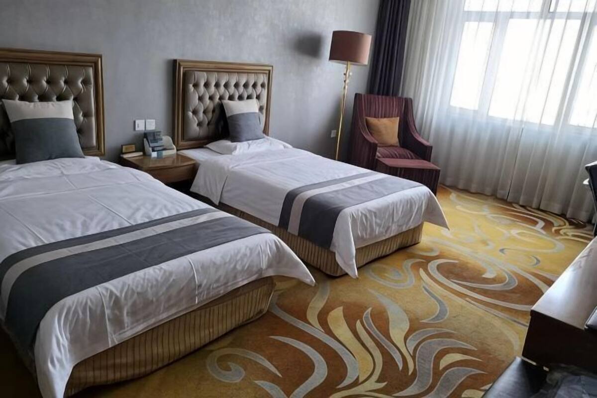 A hotel room with two beds, a nightstand, a lamp, and a chair.