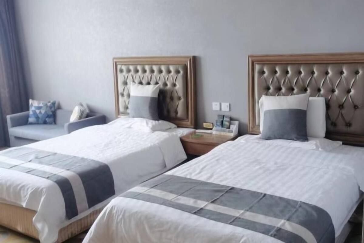 A hotel room with two beds, each with a tufted headboard, a bedside table, and a chair.