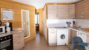 Eine moderne Küche mit Holzschränken, einer Waschmaschine und einem Essbereich mit einem Glastisch.