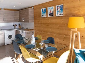 A modern kitchen with wooden cabinets, a washing machine, and a dining area with a glass table and chairs.