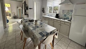 Een keuken met een eettafel, stoelen, een koelkast en een raam.