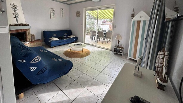 Een woonkamer met een blauwe bank, een kleine ronde tafel en een open haard. Er is een schuifdeur die leidt naar een buitenruimte met stoelen.