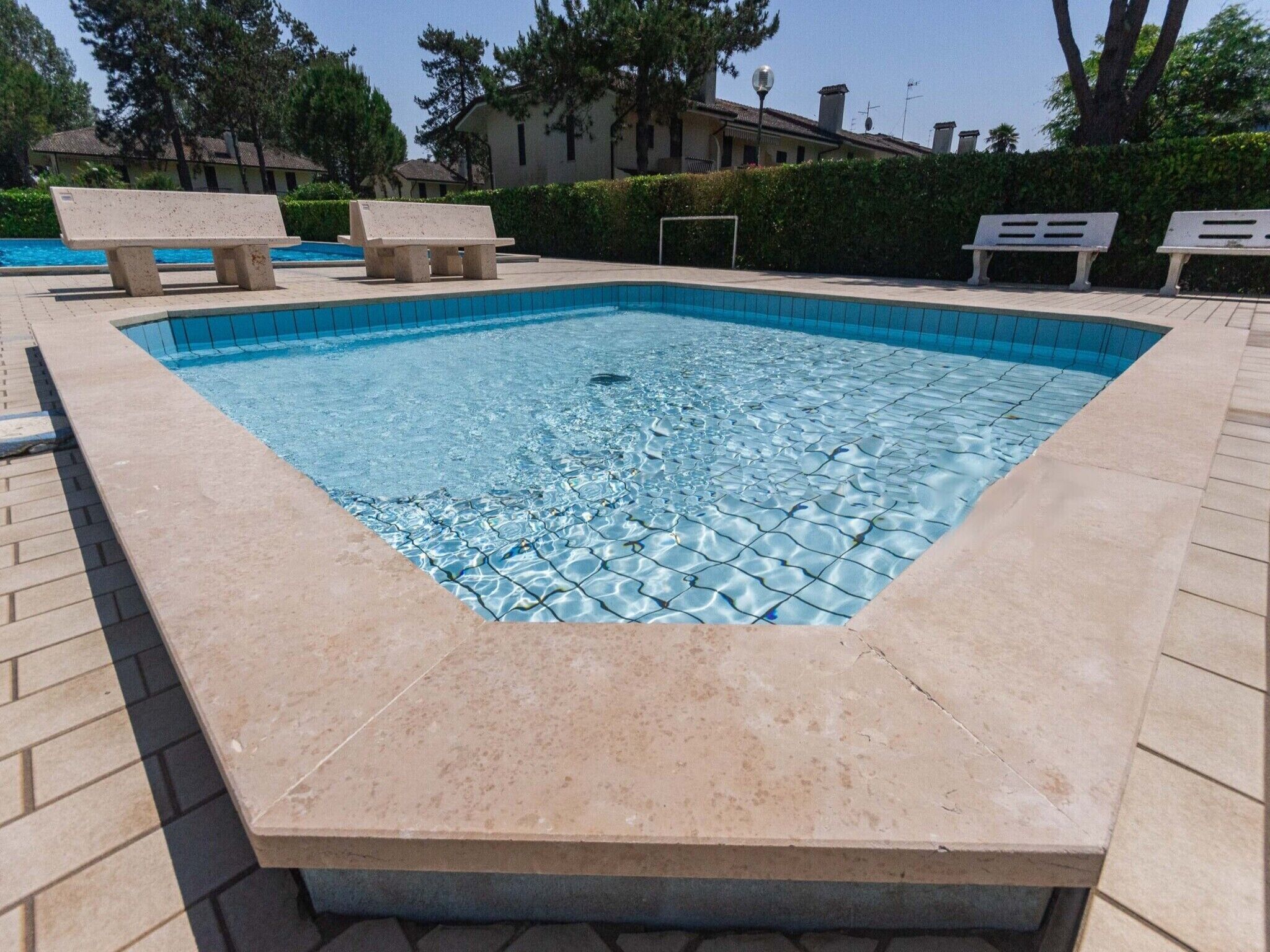 A square swimming pool with a tiled edge, surrounded by a paved deck and benches.