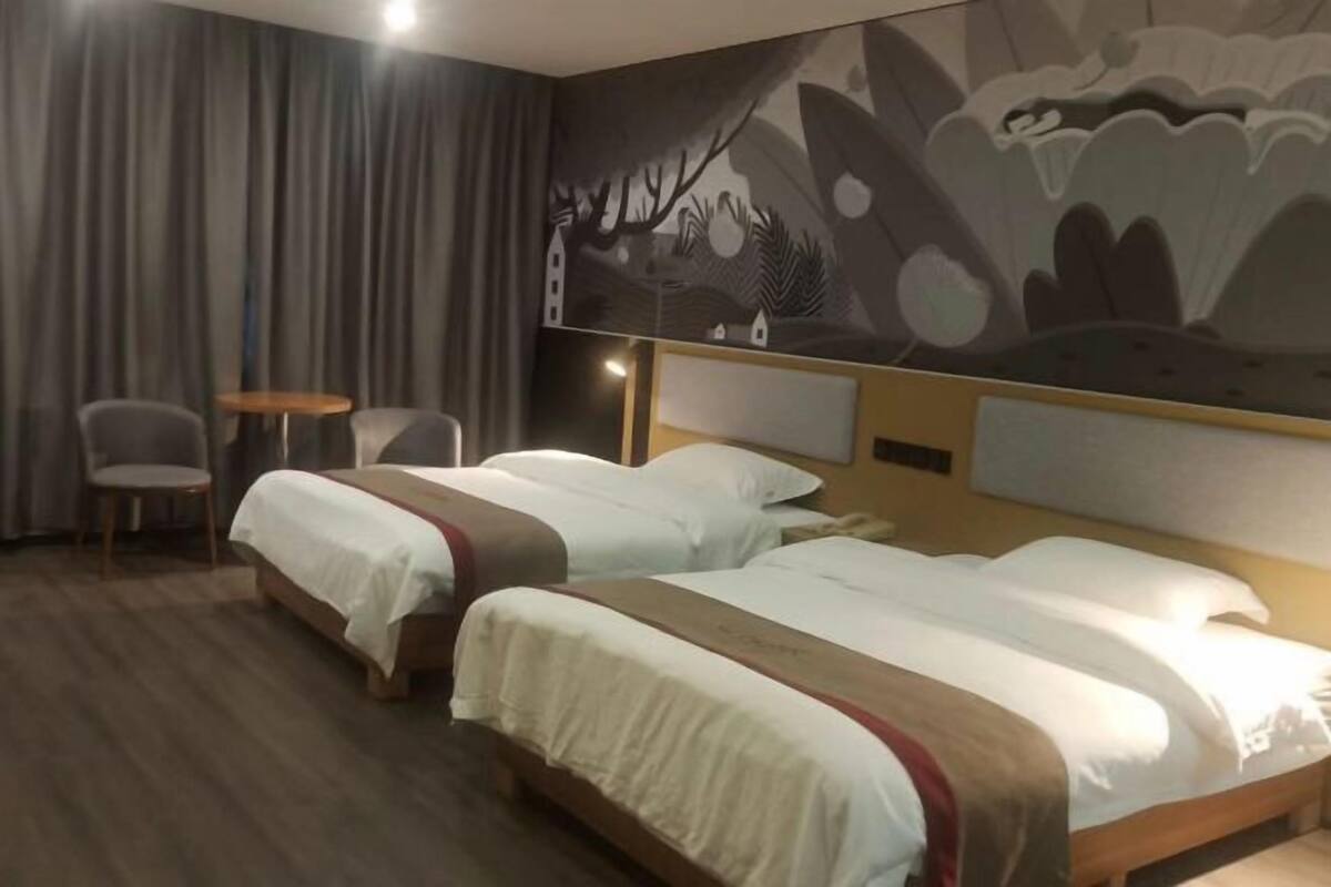 A hotel room with two beds, a small table, two chairs, and a mural on the wall.