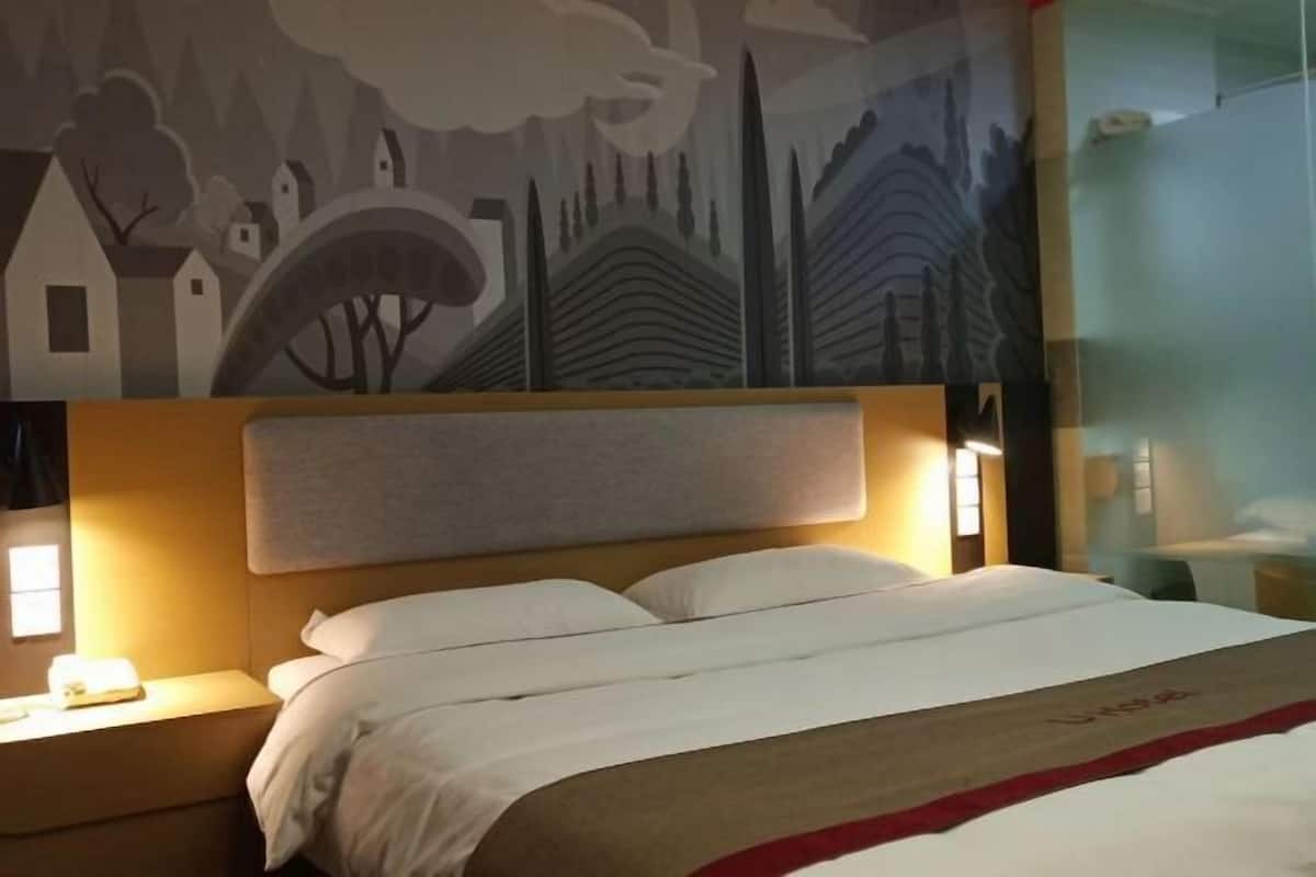 A hotel room with a large bed, a headboard, bedside lamps, and a mural on the wall.
