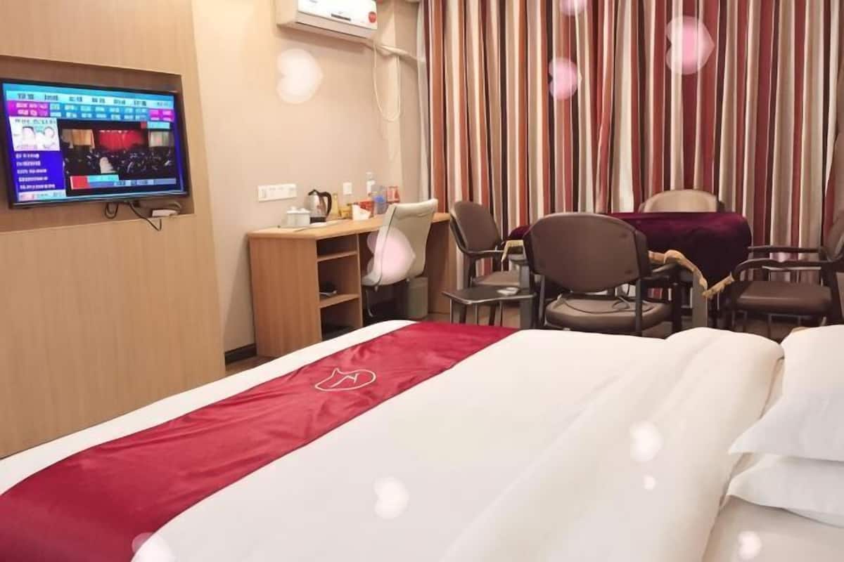 A hotel room with a bed, a desk, two chairs, a TV, and a curtain.