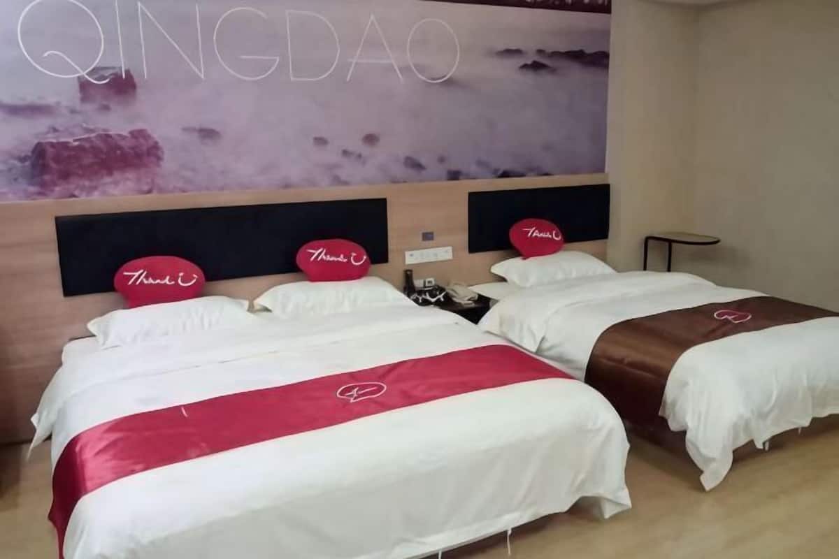 A hotel room with two beds, each with a headboard, a wall-mounted TV, and a small table.
