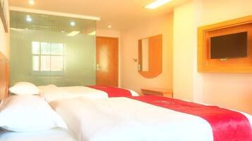 A hotel room with two beds, a TV mounted on the wall, and a glass door leading to a bathroom.