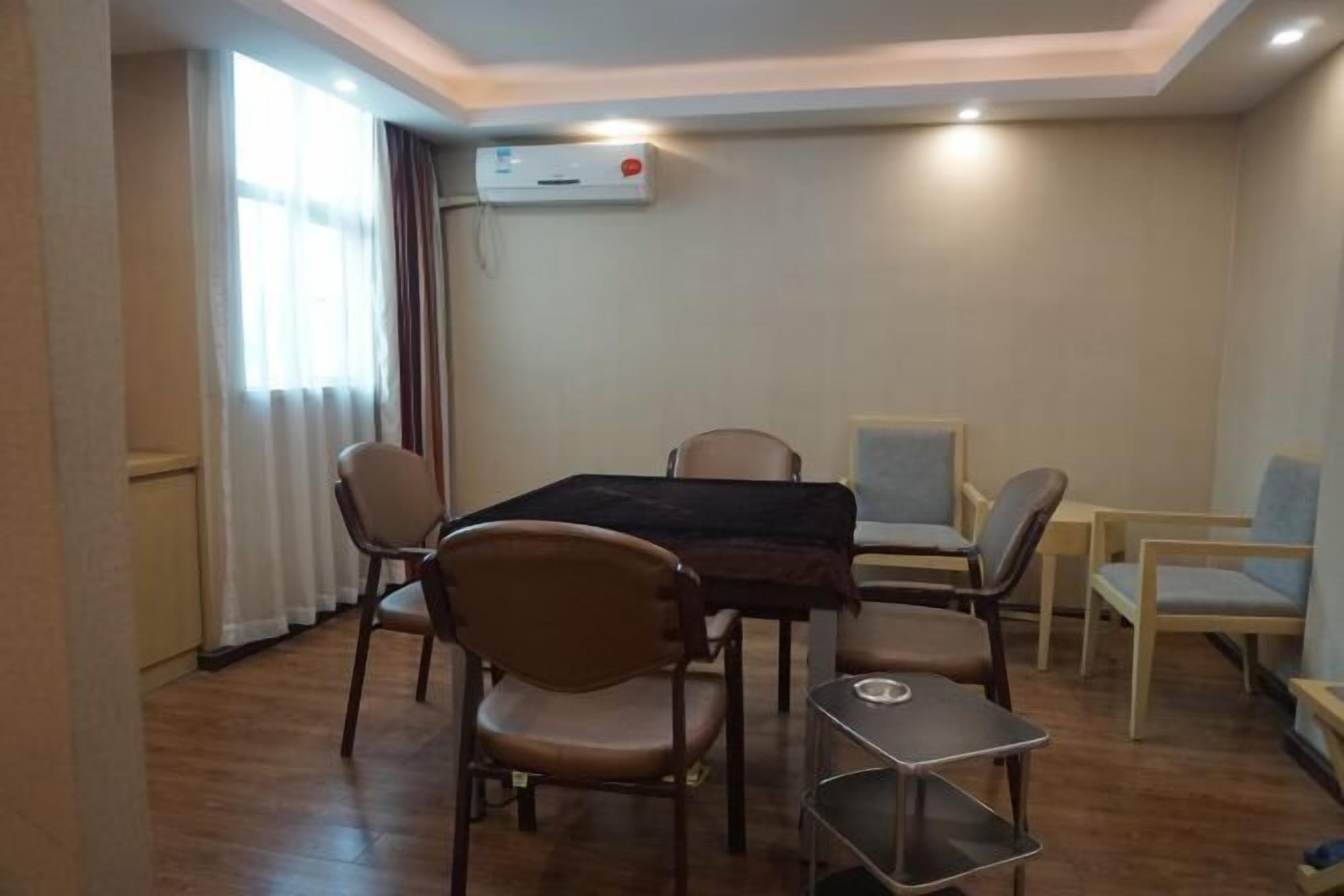 A dining area with a table and chairs, an air conditioning unit on the wall, and a window with curtains.