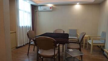 A dining area with a table and chairs, an air conditioning unit on the wall, and a window with curtains.