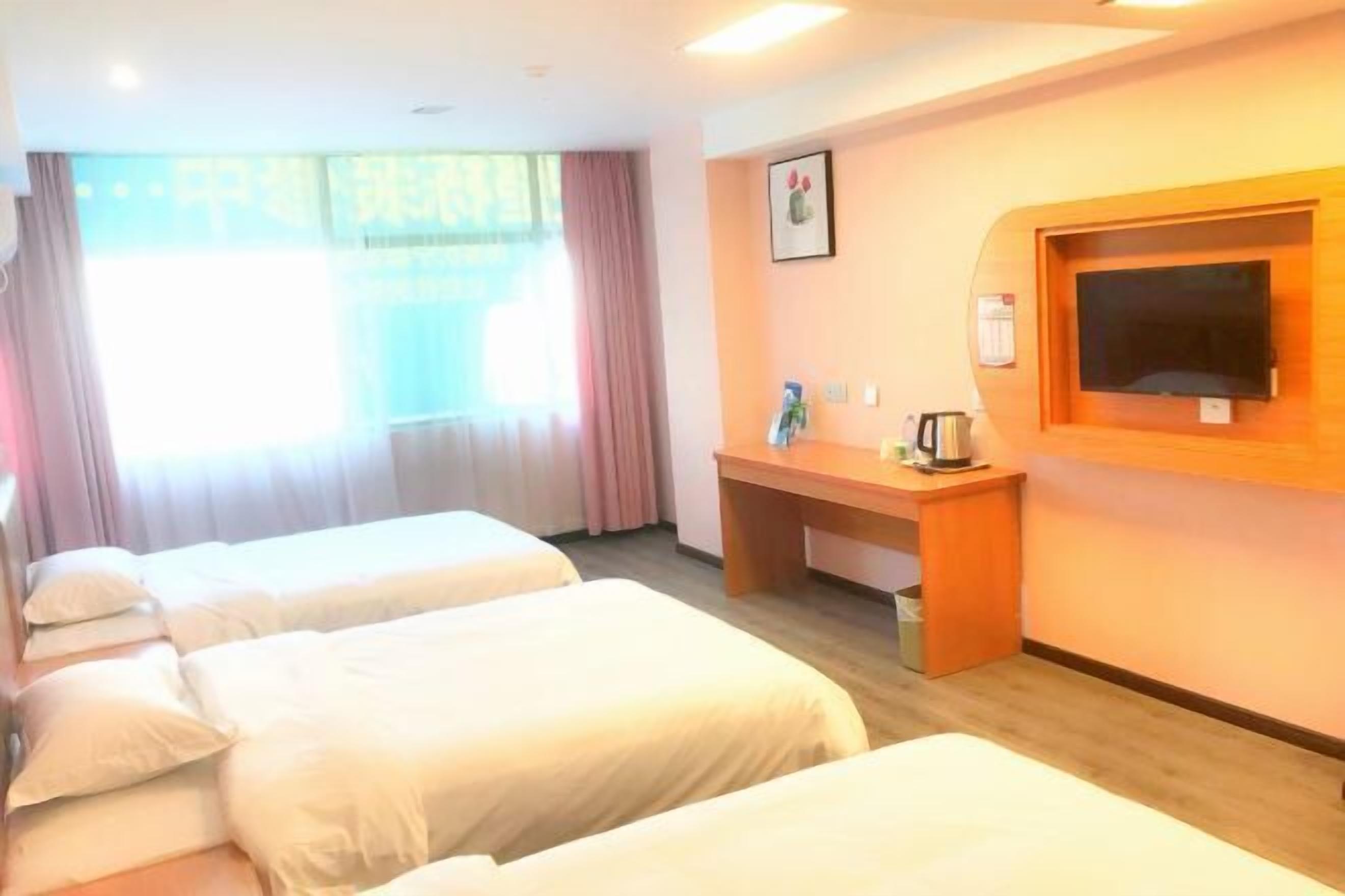 A hotel room with two single beds, a desk with a chair, a television mounted on the wall, and a window with curtains.