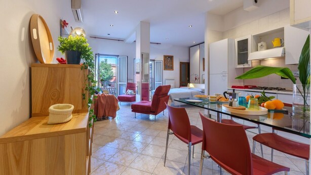 Cozinha moderna com mesa de jantar de vidro, cadeiras vermelhas e um vaso de plantas.