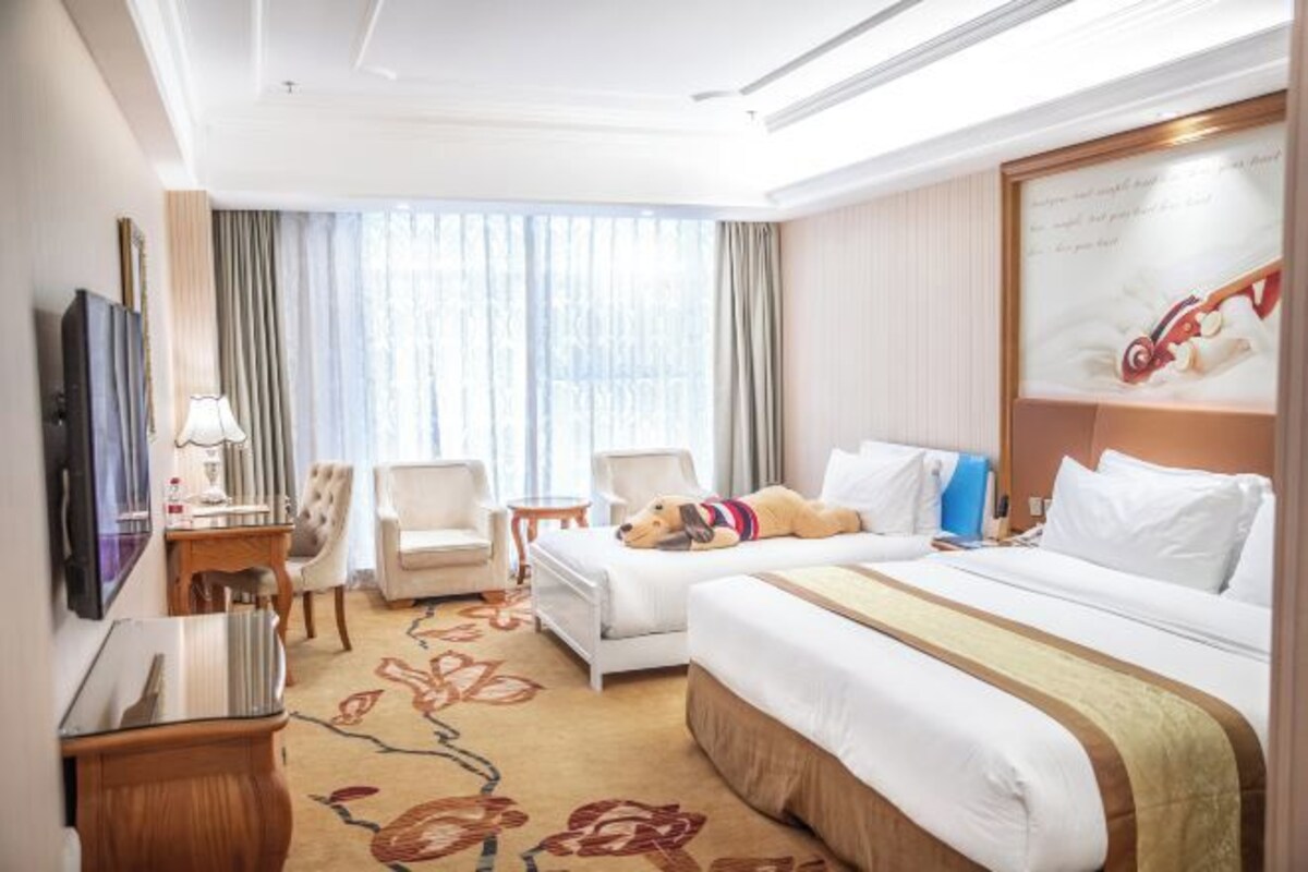 A hotel room with two beds, a TV, a desk, and a dog.