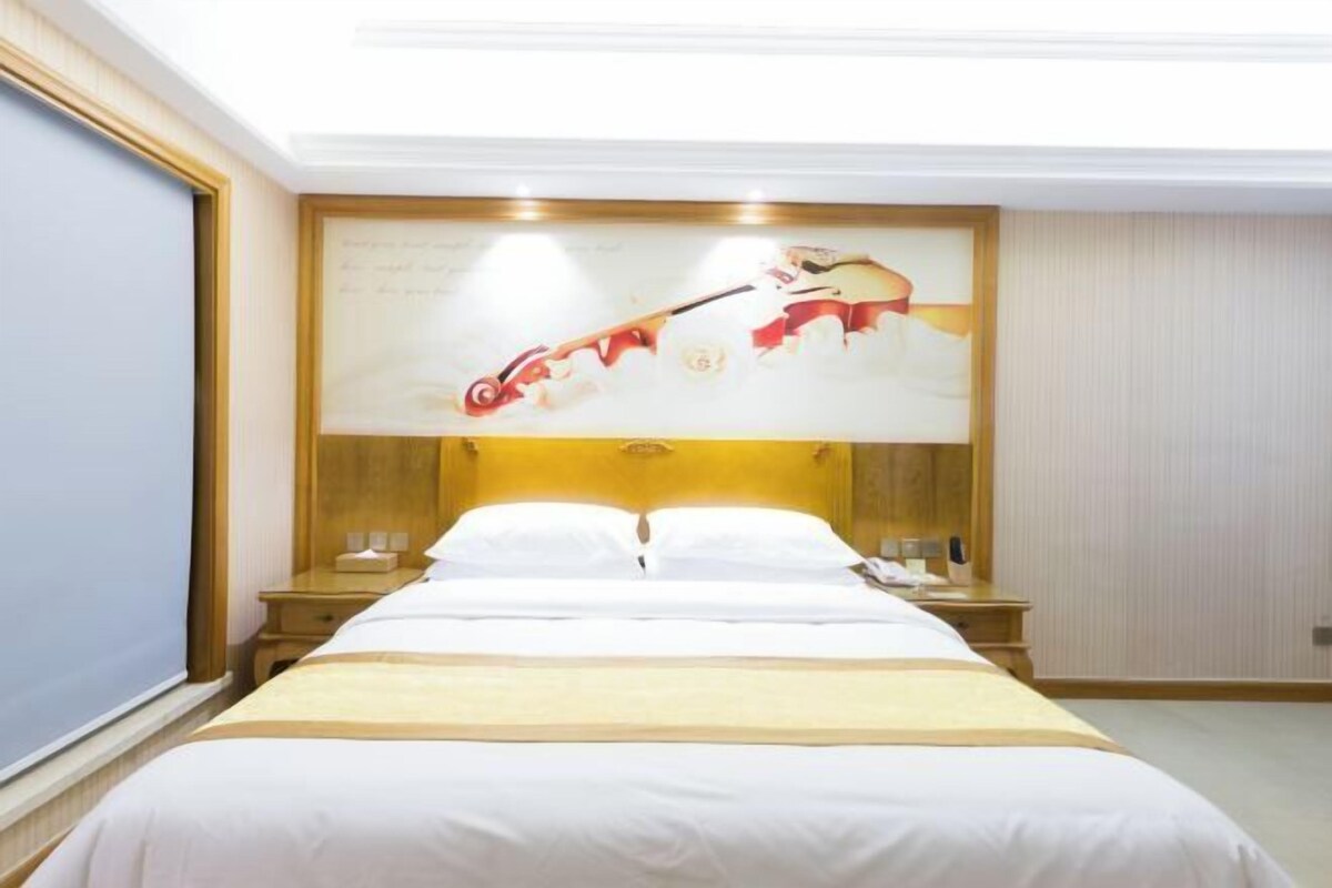 A hotel room with a large bed, two bedside tables, a nightstand, and a wall-mounted artwork.