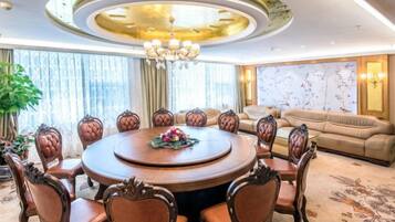 A round dining table with chairs, a chandelier, and a sofa in a well-lit room with large windows.
