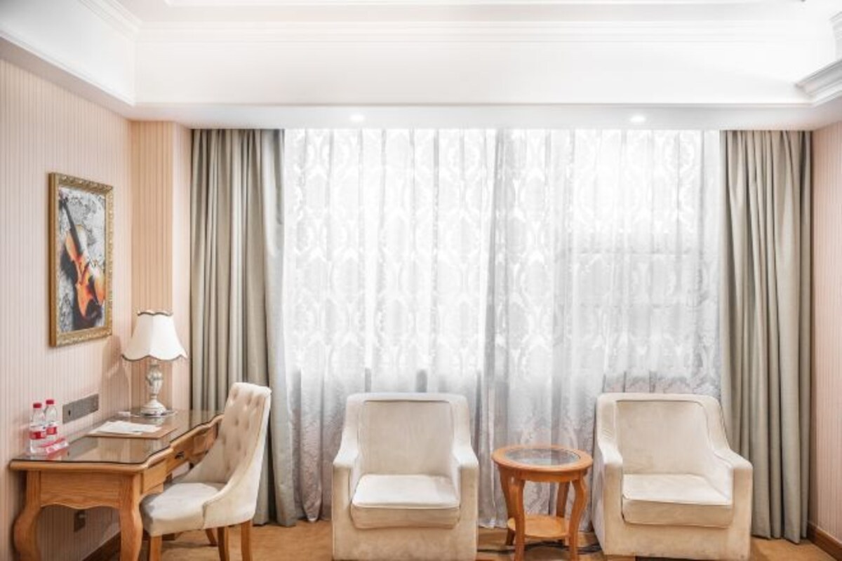 A hotel room with two armchairs, a small round table, a lamp, and a painting on the wall.