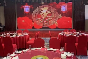 Un salón de conferencias con mesas redondas, sillas rojas y una pantalla grande mostrando caracteres chinos.