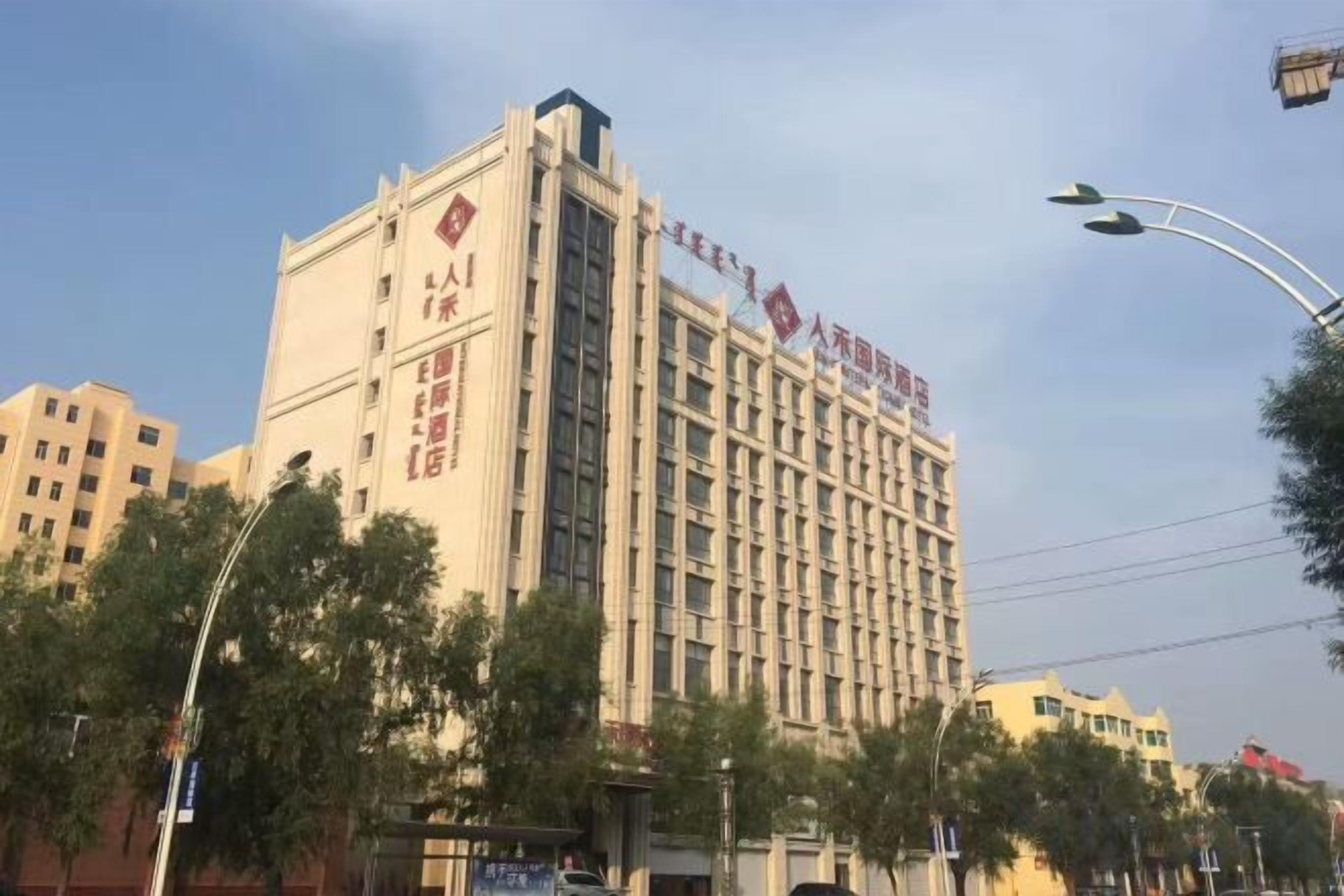 A multi-story hotel with a prominent sign on the facade, surrounded by trees and other buildings.