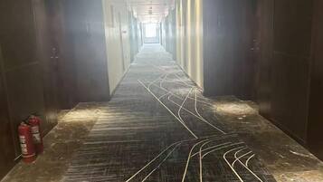 A long, narrow hallway with a patterned floor, fire extinguishers on the left, and doors on both sides.
