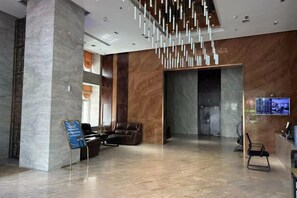 Un vestíbulo moderno con una columna de mármol, un área de descanso con sillones de cuero, una lámpara colgante y una recepción.