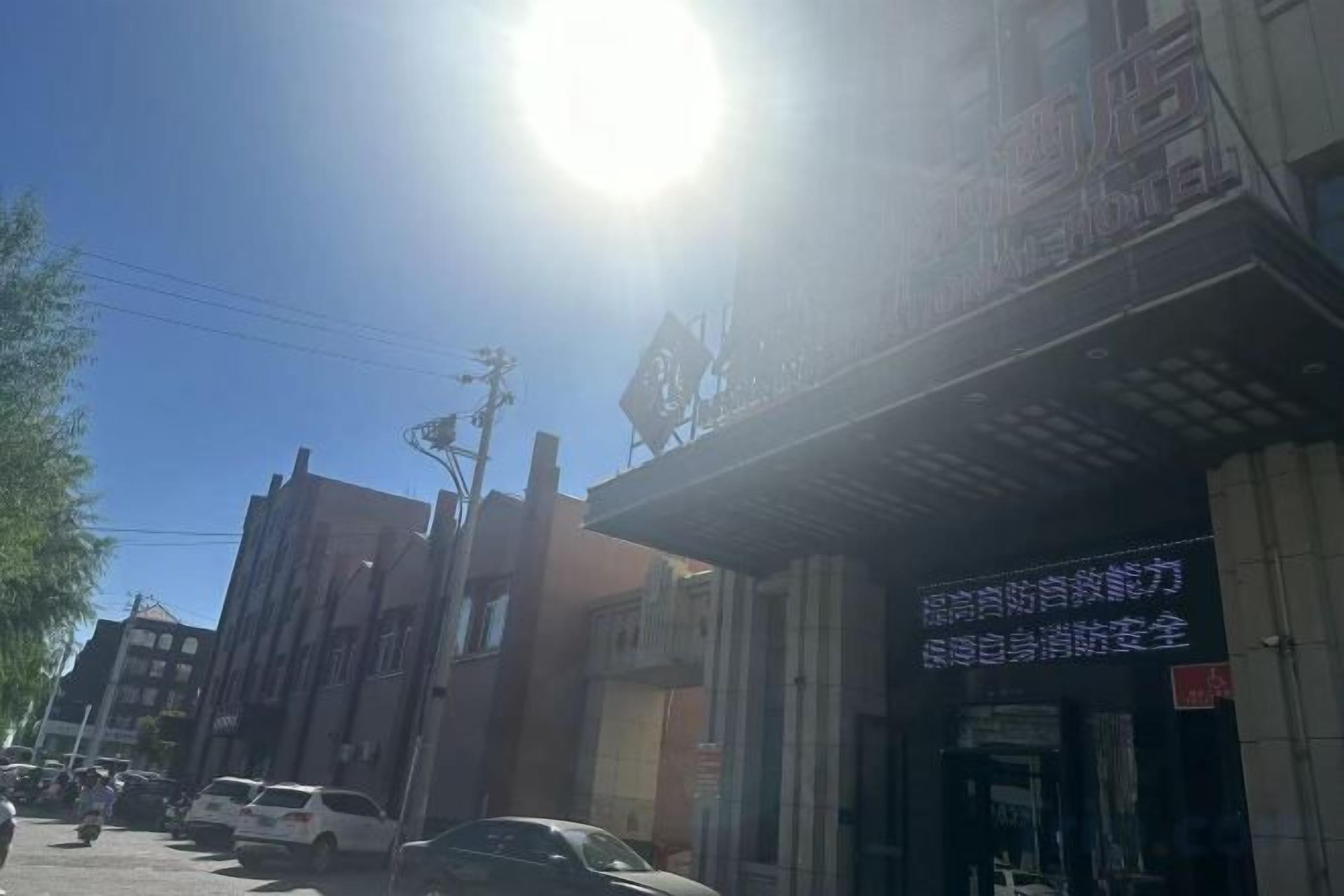 A street view with buildings, a clear sky, and a bright sun.