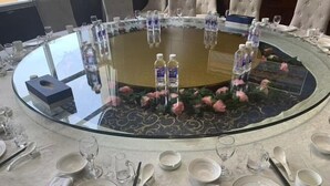 A round table with a glass top surrounded by chairs, water bottles, and a floral design. - Renhe International Hotel (Jarud Banner)