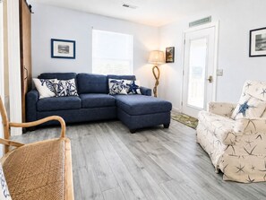 A living room with a blue sectional sofa, a beige armchair, a wooden chair, a lamp, and a door labeled 'BEACH HOUSE'. - #208 "Sandy Schus" 1 BD + Sleeper, Modern,Pool (Isle of Palms)