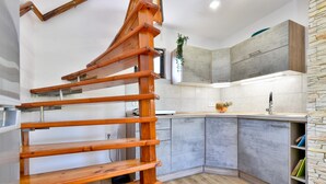 A modern kitchen with grey cabinets, a wooden staircase, and a stone accent wall.