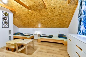 Een kleine, knusse kamer met een schuine kap, twee eenpersoonsbedden, een houten tafel en een witte ladekast.