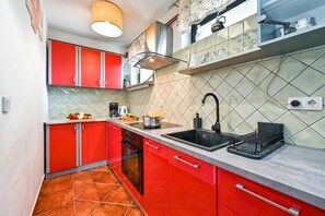 Une cuisine de taille réduite avec des meubles rouges, un évier noir et un dosseret carrelé.